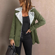 Woman wearing an army green jacket with white fleece-look lining, wide lapels and buckled cuffs over a black top and jeans