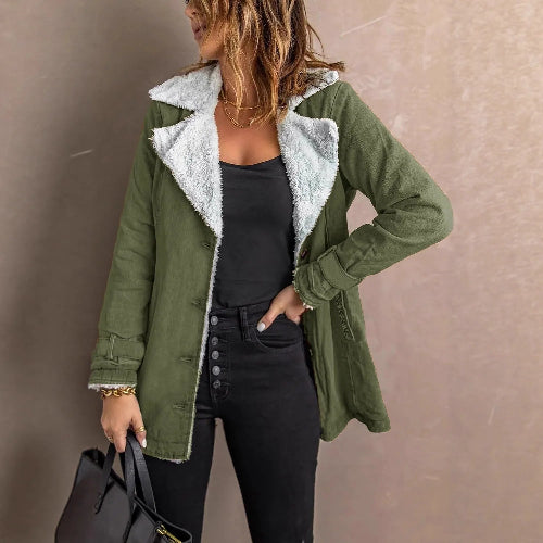 Woman wearing an army green jacket with white fleece-look lining, wide lapels and buckled cuffs over a black top and jeans