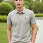 Light gray shirt with a brand logo on a hanger and being held by a hand.