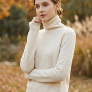 A close-up of a person wearing a fuzzy, cream-colored turtleneck sweater. The sweater has a soft, mohair-like texture and is styled with a patterned skirt.