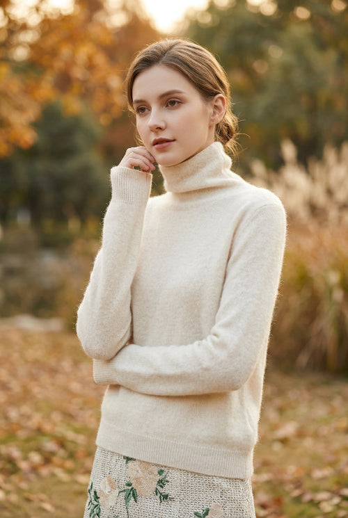 A close-up of a person wearing a fuzzy, cream-colored turtleneck sweater. The sweater has a soft, mohair-like texture and is styled with a patterned skirt.