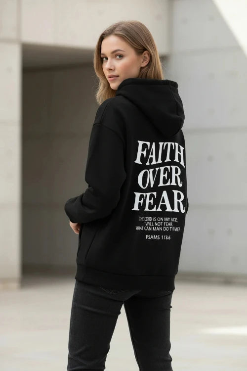 Black hoodie with 'Faith Over Fear' text on a wooden surface with shoes and headphones.