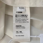 A close-up of a white fabric garment showing a sewn-in product tag with Chinese and English text including 'S(34)', material composition, and 'Made in China'.