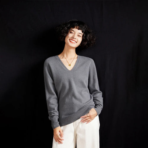 Woman wearing a gray sweater and white pants against a black background