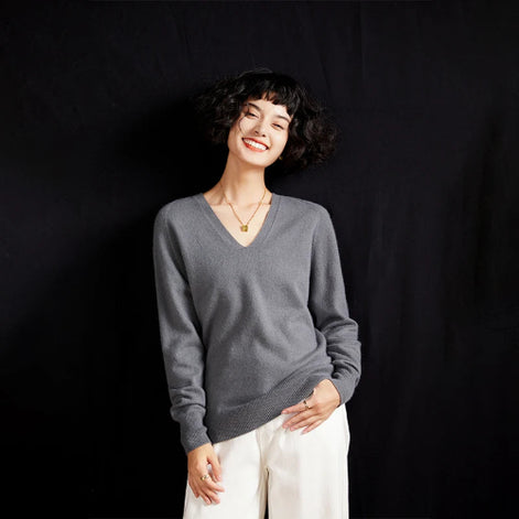 Woman wearing a gray sweater and white pants against a black background