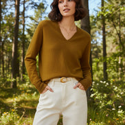 Woman wearing a mustard yellow sweater and white pants against a beige background