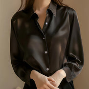 Black satin button-down shirt worn by a model with hands clasped, shown from the front.
