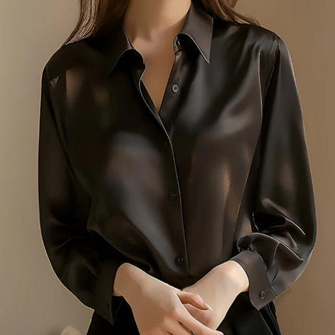 Black satin button-down shirt worn by a model with hands clasped, shown from the front.