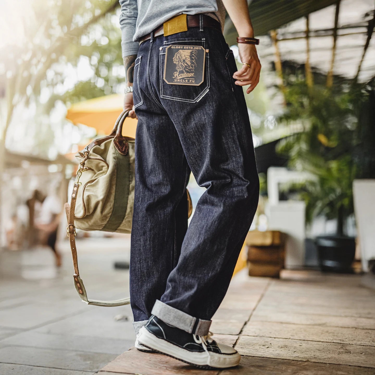 Person wearing dark blue jeans with a brand logo, holding a green bag outdoors.