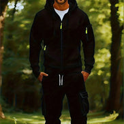 A man wearing a black zip-up hoodie and matching black cargo pants with white drawstrings, standing in a sunlit forest setting.