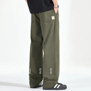 Rear view of a model wearing army green loose-fit straight-leg pants with two back patch pockets and a small sewn-on label, paired with black sneakers.