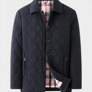 A men's quilted jacket in a very dark navy blue, featuring a diamond-stitched pattern, a pointed collar, and a plaid lining in red, white, and blue. A small black label in the top-left corner reads '望色' (meaning dark navy).