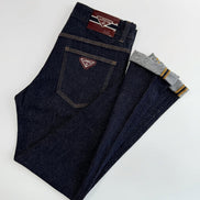 A pair of dark indigo denim jeans laid flat on a white background, with one leg folded over to show the inner cuff which has gray lining and yellow stripes. 