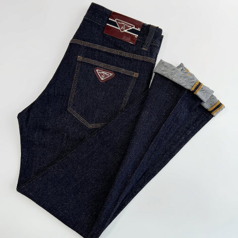 A pair of dark indigo denim jeans laid flat on a white background, with one leg folded over to show the inner cuff which has gray lining and yellow stripes. 