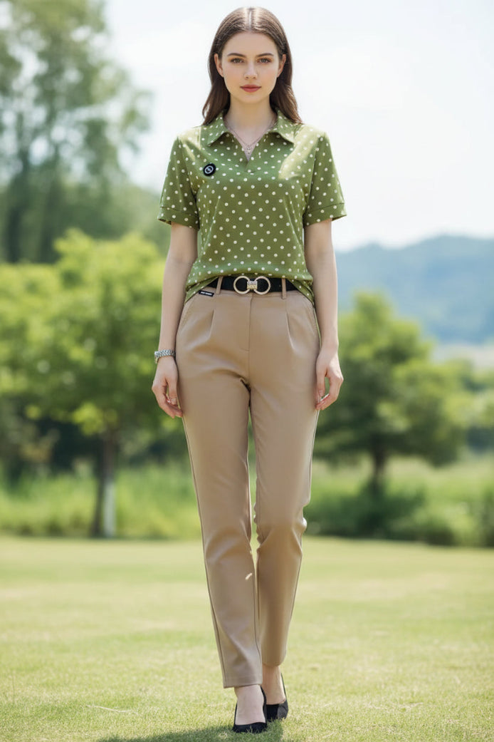 A woman wearing a short-sleeve olive green polo shirt with white polka dots, paired with beige trousers and a black belt with a silver buckle.
