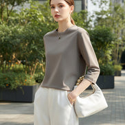 Person wearing a light gray long-sleeve top and white pants, holding a handbag.