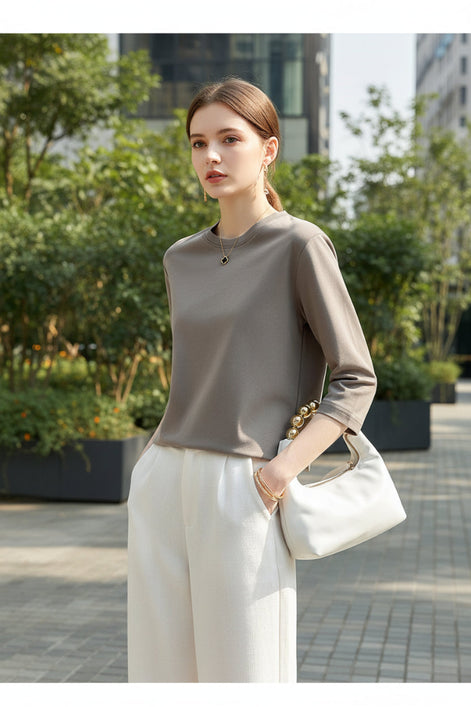 Person wearing a light gray long-sleeve top and white pants, holding a handbag.
