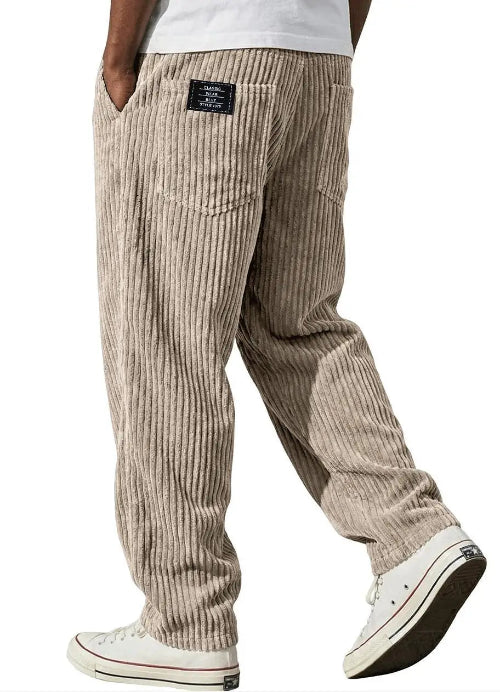 A person wearing beige corduroy pants with a vertical ribbed texture, shown from the waist down against a plain white background. 