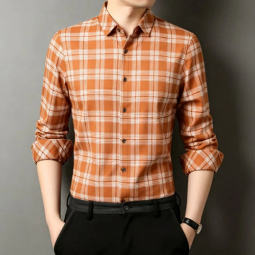 A man wearing a long-sleeve button-up plaid shirt in orange and white, paired with black trousers, shown from the chin down against a dark gray background.