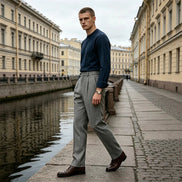 Gray herringbone pleated suit trousers worn by a man walking along a canal