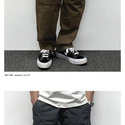 Front views of a model wearing brown and dark gray cargo pants, showing thigh pockets, curved seam detailing, and stitched knee panels.