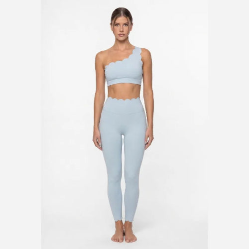 Woman wearing a light blue one-shoulder top and leggings on a white background