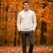Folded cream-colored sweater with a watch on a gray surface