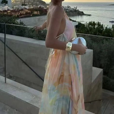 Woman in a colorful dress standing on a balcony with a scenic view of water and buildings.