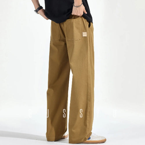 Rear view of a model wearing khaki loose-fit straight-leg pants with two back patch pockets and a small sewn-on label, paired with white sneakers.