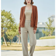 A woman seated indoors wearing a fuzzy open-front cardigan in a warm camel-brown color over a cream ribbed top. The i