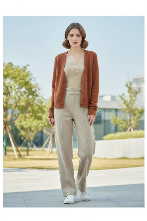 A woman seated indoors wearing a fuzzy open-front cardigan in a warm camel-brown color over a cream ribbed top. The i