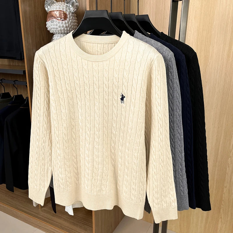 Beige cable knit sweater with a brand logo on a rack with other sweaters.