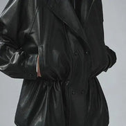 Close-up of a black faux leather jacket showing the gathered waist, snap-button front and sleeve detailing with hands in the pockets