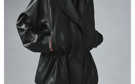 Close-up of a black faux leather jacket showing the gathered waist, snap-button front and sleeve detailing with hands in the pockets