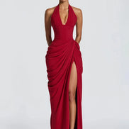 A woman modeling a floor-length red halter gown with a deep plunging neckline, gathered draped detailing, and a high thigh slit, 
