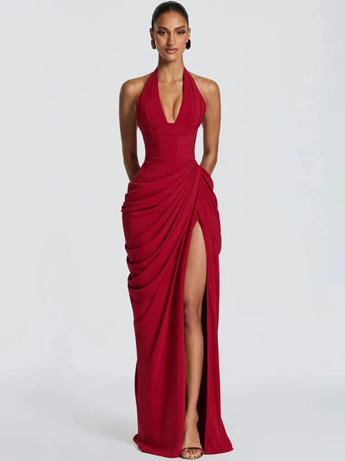A woman modeling a floor-length red halter gown with a deep plunging neckline, gathered draped detailing, and a high thigh slit, 