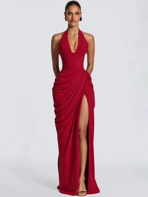 A woman modeling a floor-length red halter gown with a deep plunging neckline, gathered draped detailing, and a high thigh slit, 