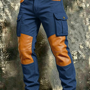 Blue cargo pants with tan contrast panels at the knees and front pockets, flap thigh pockets, and a brown belt against a textured gray background.