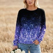 A woman wearing a long-sleeve crewneck top covered in sequins that fade from black at the top to bright blue and purple at the bottom, paired with distressed blue jeans 