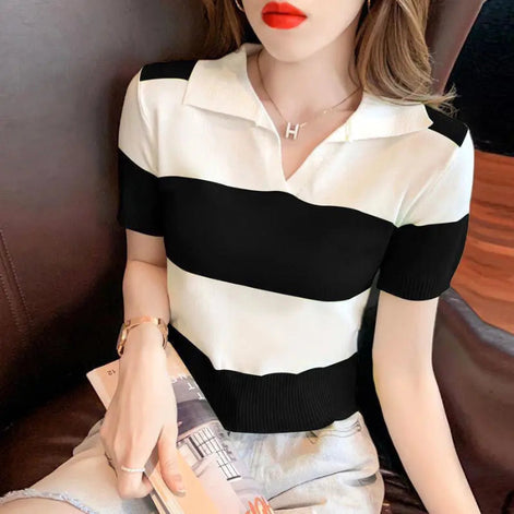 A woman wearing a short-sleeve knit polo shirt with bold black and off-white horizontal stripes, seated on a dark brown leather couch and holding a magazine.
