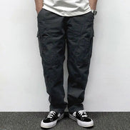 Front view of a model wearing dark gray loose-fit cargo pants with thigh pockets, curved seam detailing, and stitched knee panels, paired with black sneakers.