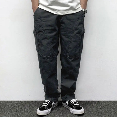 Front view of a model wearing dark gray loose-fit cargo pants with thigh pockets, curved seam detailing, and stitched knee panels, paired with black sneakers.