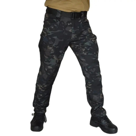 Front view of a model wearing dark camouflage cargo pants with a black belt and black lace-up boots against a white background.