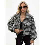 Woman wearing a black and white houndstooth utility jacket with chest flap pockets, a ring-pull zipper and drawcord hem over a black top and trousers