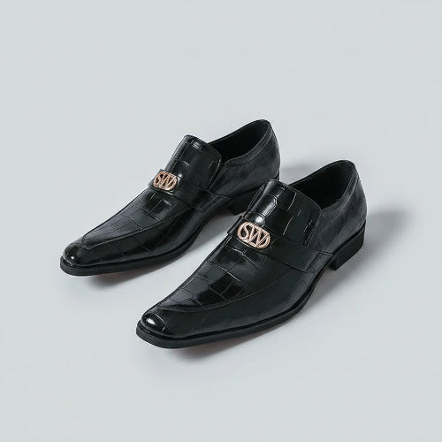 Black dress shoes with gold logo worn by a person on a white background