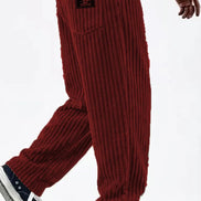 A person wearing loose ribbed knit pants in deep red, paired with a white shirt and black-and-white sneakers, shown from the waist down 