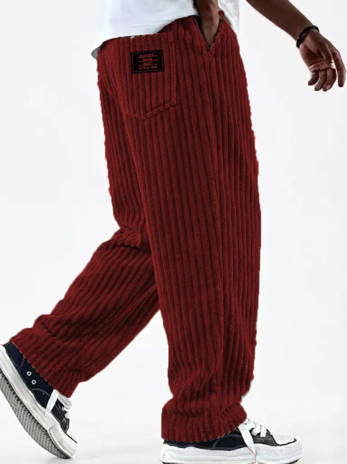 A person wearing loose ribbed knit pants in deep red, paired with a white shirt and black-and-white sneakers, shown from the waist down 