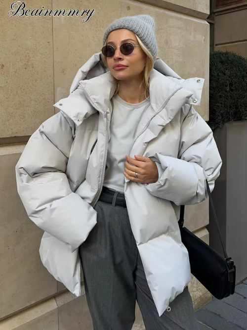 Woman wearing a light gray hooded puffer jacket open, showing a wide padded collar, front zipper and voluminous long sleeves