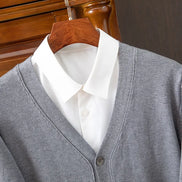 Gray cardigan over a white shirt on a wooden hanger against a wooden door background