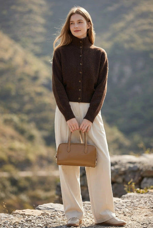 A person taking a mirror selfie wearing a dark brown mock-neck knit cardigan, a cream pleated skirt, and carrying a tan leather handbag.